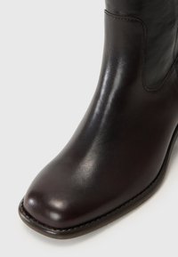 Brune lærre ankle boot med en rund tå, glat tekstur, subtil glans og kontrasterende søm langs sålen. Har elastiske paneler.