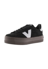 Zapatillas de ante negro con un logo en V blanco, cordones planos y una gruesa suela de goma marrón. La textura es suave y con un ligero brillo.