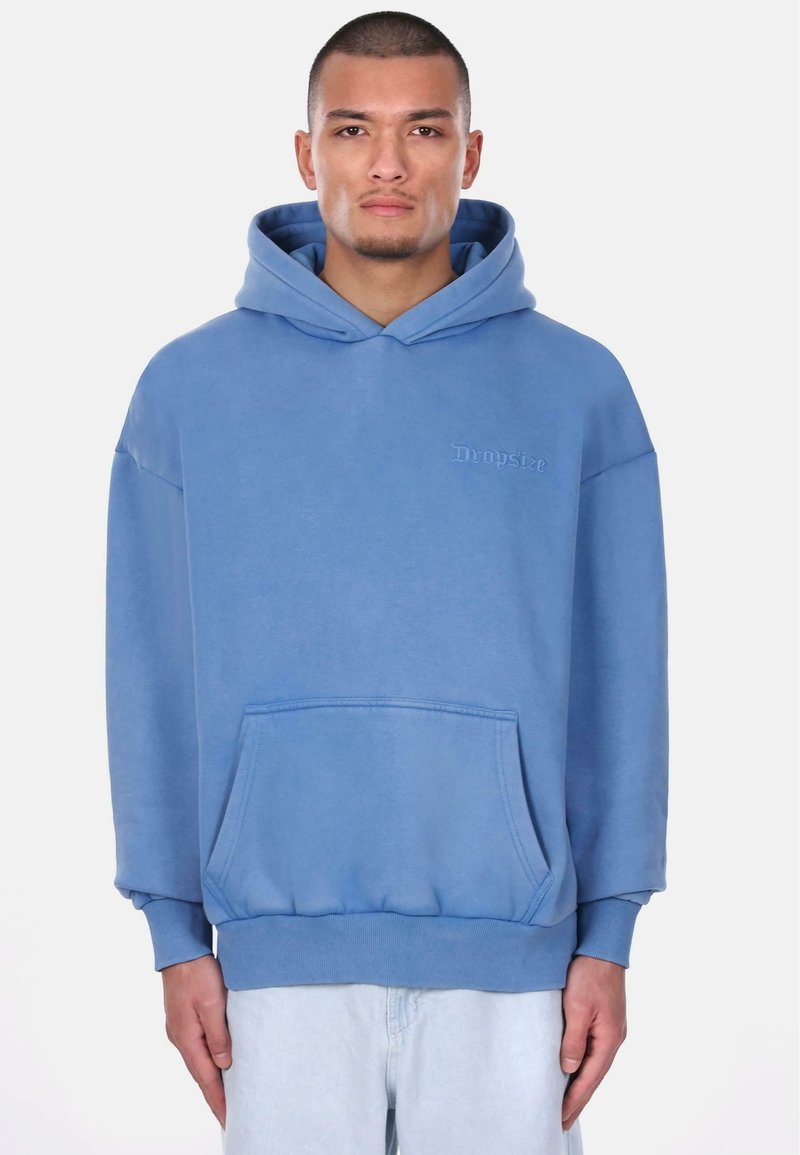 Lyseblå hoodie lavet af blødt stof. Har en frontlomme, ribbede manchetter og diskret logo-broderi på brystet.