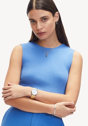 Top blu ribbed senza maniche, collane d'oro a strati con pendenti a forma di cuore, bracciale in argento e un orologio con quadrante bianco e cinturino beige.