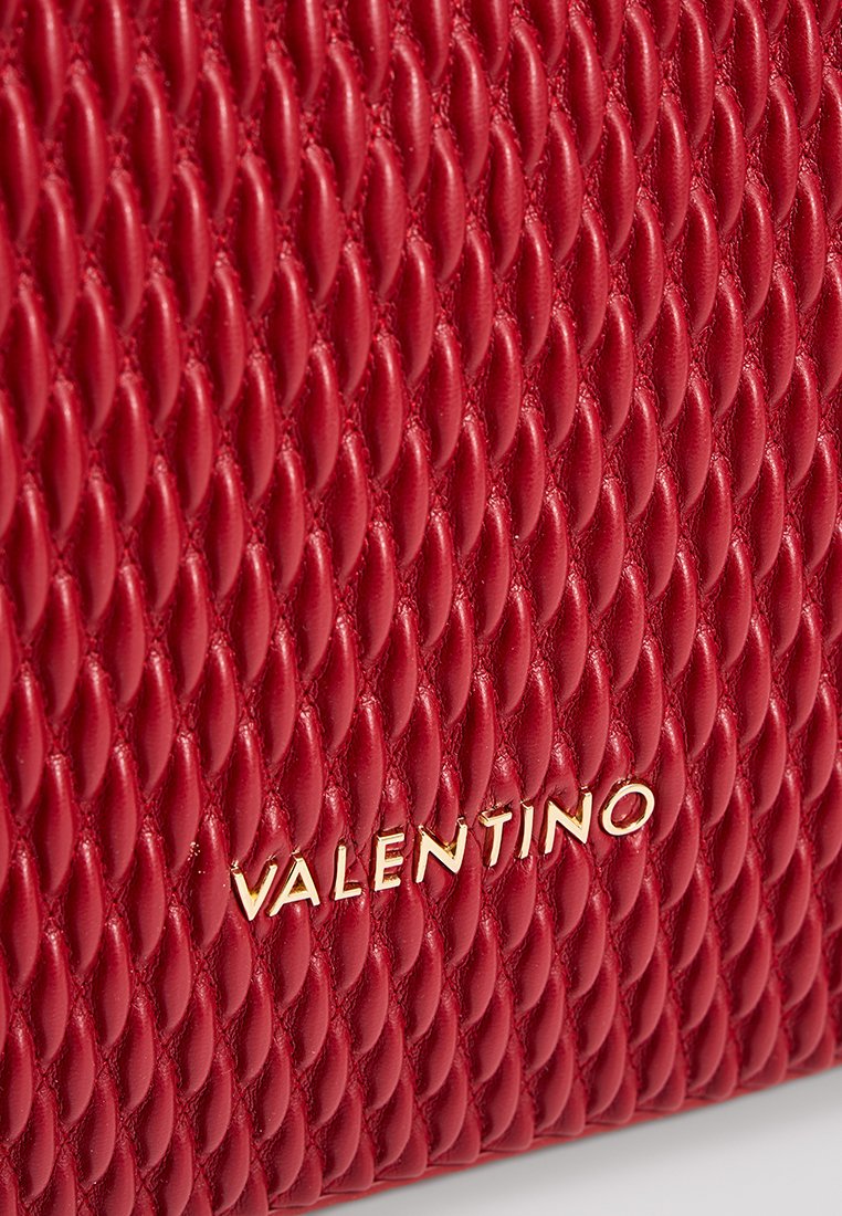 Sac en cuir rouge avec un motif en losanges matelassé. Présente la marque dorée "VALENTINO" en bas à droite. La surface texturée ajoute de la dimension.