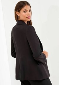 Sacou negru, croi pe măsură, dintr-un material neted, având guler cu tăietură, mâneci lungi și un detaliu cu un singur nasture la mansetă.