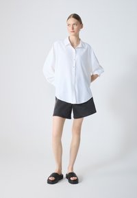 White button-up shirt with a relaxed fit, paired with black denim shorts and black platform sandals. Smooth fabric, minimal design, and no patterns.