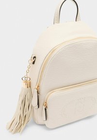 Zaino in pelle crema con forma arrotondata, zip dorata, nappina laterale e una tasca frontale con dettaglio embossato. Design minimalista.