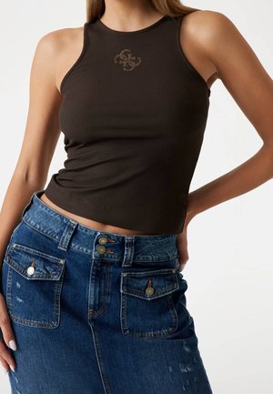 Kvinde iført en tætsiddende sort ærmeløs top med et lille dekorativt logo og en højtaljet blå denimskørt med frontlommer.