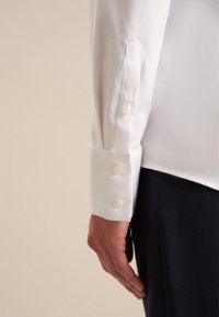 Witte, gestructureerde shirtmouw met een afgeronde manchet met drie witte knopen en een getailleerde pasvorm, gecombineerd met donkere broek.