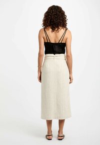 Camisón de satén negro con tirantes finos, combinado con una falda midi a rayas beige que presenta un lazo en la parte trasera y una textura suave.