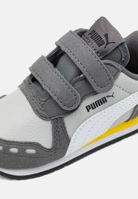 Gray and white Puma sneaker with double velcro straps, black Puma logo on side and tongue, and a yellow accent on the sole.