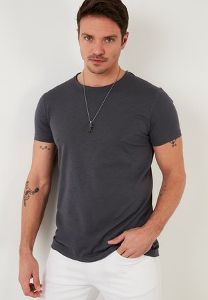 T-shirt grigio a maniche corte realizzato in morbido tessuto. Scollo rotondo e vestibilità slim, con tatuaggi sulle braccia e una collana.