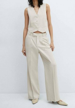 Gilet beige slim sans manches avec boutons, associé à un pantalon beige taille haute à jambes larges et des chaussures assorties à bout pointu.