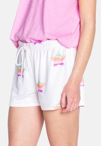 Pantalones cortos blancos con un patrón de estrellas coloridas en tonos pastel, con una cinturilla elástica y cordón. Llevados con una blusa rosa.