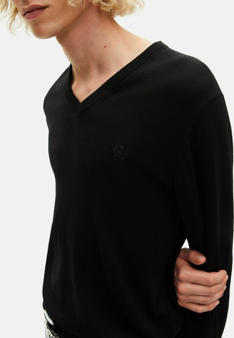 Pull-over noir en v, fabriqué à partir d'un matériau en tricot doux. Présente un logo subtil sur la poitrine et une coupe décontractée avec des manches longues.