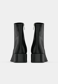 Bottes basses noires en cuir lisse avec un talon géométrique, dotées d'une fermeture éclair discrète au dos et d'une silhouette épurée.