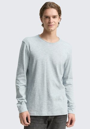 Helles blaues Langarm-T-Shirt mit weichem Textil, rundem Ausschnitt und minimalistischem Design, kombiniert mit dunklen Jeans.