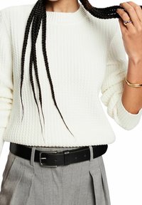 Maglione bianco a coste con scollo rotondo, abbinato a pantaloni grigi chiari a pieghe e una cintura in pelle nera con fibbia argentata.