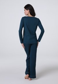 Completo loungewear verde acqua con maniche lunghe e pantaloni, realizzato in tessuto morbido. Presenta un collo semplice e cuciture a contrasto lungo i bordi dei pantaloni.