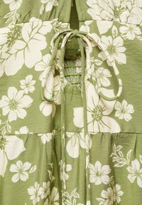 Tissu vert avec un grand imprimé floral blanc et un détail nœud noué sur une couture froncée.