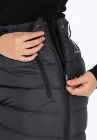 Mustapuffihame, jossa on vaakasuora tikattu kuvio. Varustettu vetskareilla ja sivutaskuilla. Materiaali näyttää sileältä ja eristetyltä.