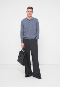 Graues Poloshirt mit Kragen und drei Knöpfen, kombiniert mit lockeren, dunkelgrauen Hosen. Schwarze Tasche mit Griffen. Einfaches, klares Design.