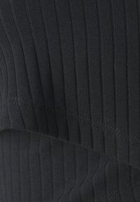 Schwarzer gerippter Stoff mit vertikalen Linien, der eine glatte Textur und gleichmäßige Nahtdetails entlang der Kanten aufweist.