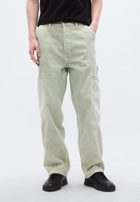 Ανοιχτό πράσινο παντελόνι cargo με φαρδιά γραμμή, φτιαγμένο από υφή υφάσματος, με πλαϊνές τσέπες και άνετη εφαρμογή, σε συνδυασμό με μ αύρα αθλητικά παπούτσια.