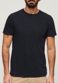 T-shirt blu navy a maniche corte realizzato in tessuto morbido, con scollatura rotonda e un piccolo accento arancione sulla manica sinistra.
