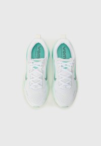 Baskets blanches de sport avec une tige en mesh, des accents verts et une semelle texturée. Comprend des lacets et une petite languette à l'arrière.