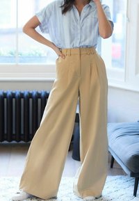 Chemise à manches courtes rayée bleu clair et pantalon beige taille haute à jambes larges, fabriqués en tissu lisse, avec un devant plissé et des poches latérales.