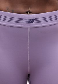 Κοντινό πλάνο της μέσης με λεβαντίν κοπής κολάν New Balance, με ορατή ραφή και σκουλαρίκι στον αφαλό.