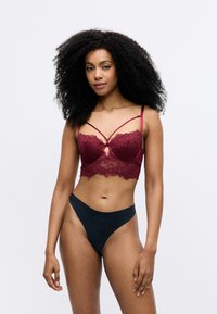 Burgundy pitsi bralette, mille kergelt disainitud rihmadega, võtmeaugu detail ja laineline ääreosa; koos mustade sujuvate kõrge vöökohtadega aluspükstega.