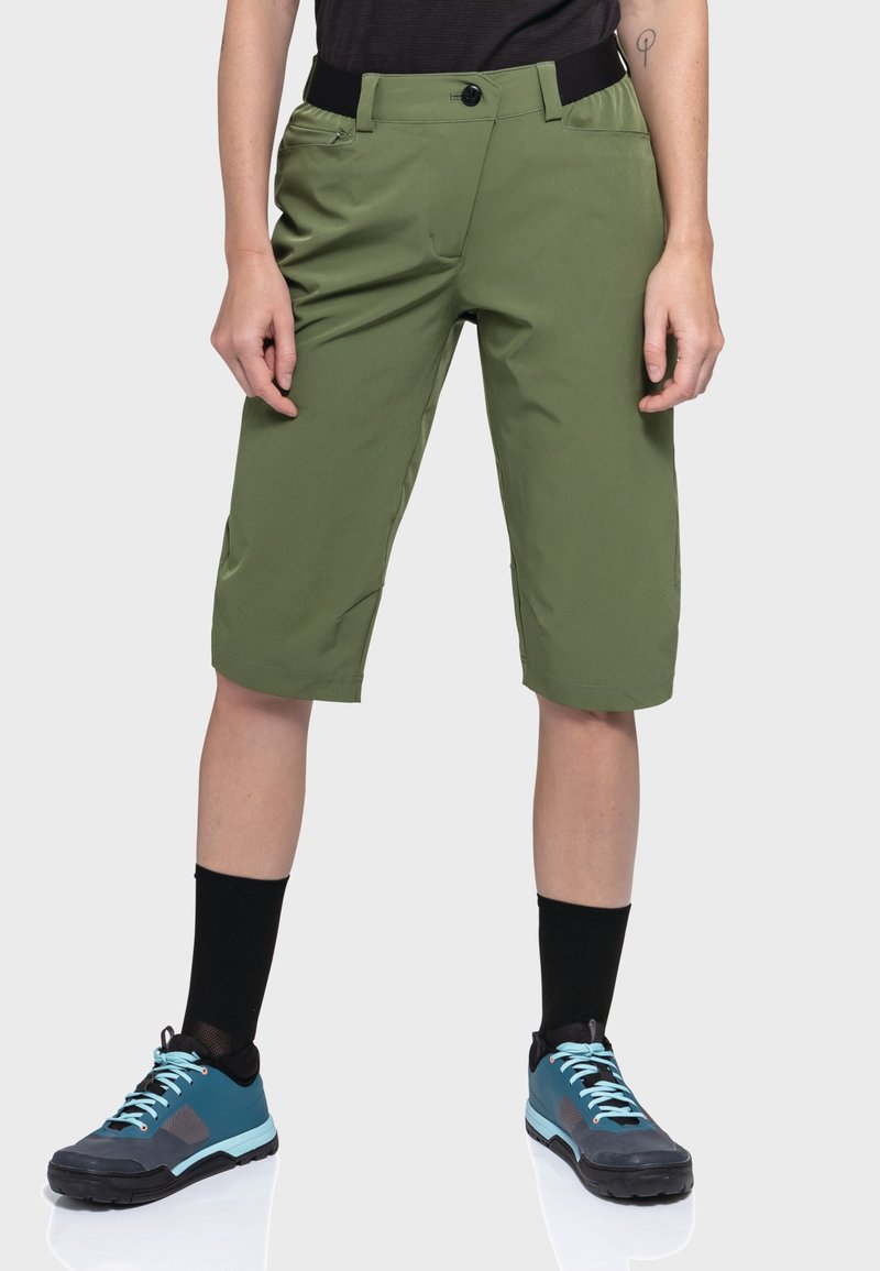 Grüne Shorts mit lockerem Schnitt, ausgestattet mit einem schwarzen Bund und Taschen, kombiniert mit schwarzen Socken und grau-blauen Schuhen.