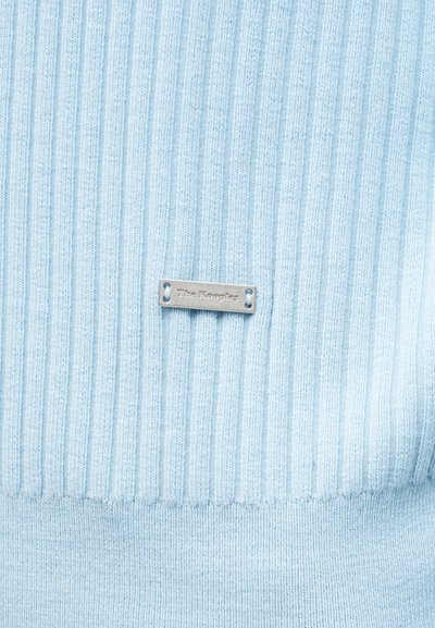 Tissu bleu clair côtelé avec une petite étiquette métallique rectangulaire centrée, gravée du nom de la marque "The Kooples".