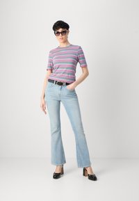 Camiseta de manga corta a rayas en rosa, azul y verde, combinada con vaqueros de campana de lavado claro y zapatos de tacón grueso negros. Cinturón negro como acento.