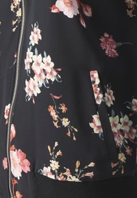Černá křiváková bunda s květinovým vzorem, zahrnující růžové a broskvové květy, stříbrný zip, žebrované manžety a boční kapsu. Hladká textura tkaniny.