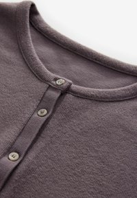 Zbliżenie na brązowy wełniany kardigan z dekoltem i trzema małymi guzikami wzdłuż przedniej listwy guzikowej.