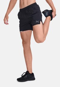 Shorts deportivos negros con un acabado texturizado, cinturilla elástica y aberturas laterales para mayor movilidad, combinados con zapatillas de entrenamiento negras.