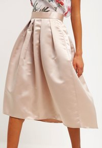 Béžová saténová midi sukně s plisováním, s přiléhavým pasem a splývavým siluetou, s hladkým povrchem a jemným leskem.