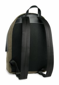 Zaino con schienale in rete nera, corpo in tessuto verde oliva e spallacci neri con dettagli in cucitura bianca. Design compatto ed ergonomico.