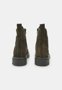 Bocanci din piele suedes maro, cu fermoar pe lateral, cusături contrastante și o talpă groasă din cauciuc negru. Vedere din spate evidențiază detaliile cusăturilor.