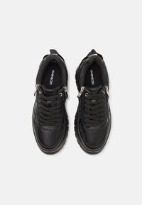 Baskets noires avec une tige en matériaux mixtes, dotées de fermetures éclair sur les côtés, de lacets et d'une semelle extérieure en caoutchouc épaisse. Détails de design texturés présents.