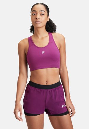 Purple sports bra and shorts set. Bra features racerback design; shorts have black waistband and FILA logo in white. Smooth texture.