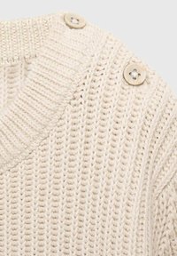 Strickpullover in Creme mit einem gerippten Muster, der zwei dekorative Knöpfe an der Schulter hat. Der Stoff wirkt weich und dehnbar.