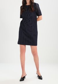 Abito blu navy con ritagli geometrici, maniche corte, scollatura rotonda e tessuto morbido. Abbinato a tacchi neri a punta.