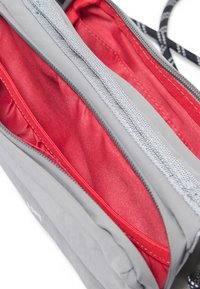Deux compartiments zippés ouverts d’un sac gris et rouge montrant l’intérieur en tissu rouge et des coutures détaillées.
