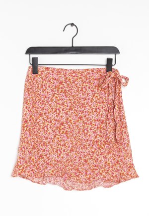 Mini falda floral en un perchero negro. Hecha de un tejido ligero y texturizado; base rosa con patrones florales en naranja y magenta; dobladillo con volantes.