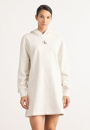Robe sweat à capuche beige avec manches longues, arborant un logo discret sur la poitrine et une coupe décontractée. Matière en mélange de coton.