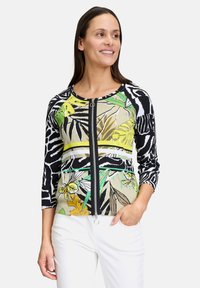 Ritssluitingjack met zwart-witte pat gepatterne mouwen, tropische bladprints in groen en geel, en een soepele textuur.
