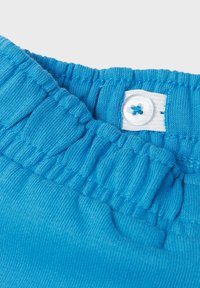 Türkiser Baumwollstoff für Kleidung mit gerafftem elastischem Taillenbund und einem weißen Knopfverschluss mit blauer Fadendetail.