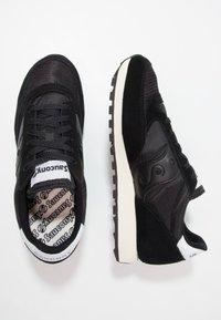 Black sneakers made of mesh and suede, featuring a white rubber sole, lace-up design, and a logo on the tongue and heel.
