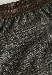 Woven fabric shorts with a brown elastic waistband, featuring a herringbone pattern in gray and cream tones, and a single back pocket.